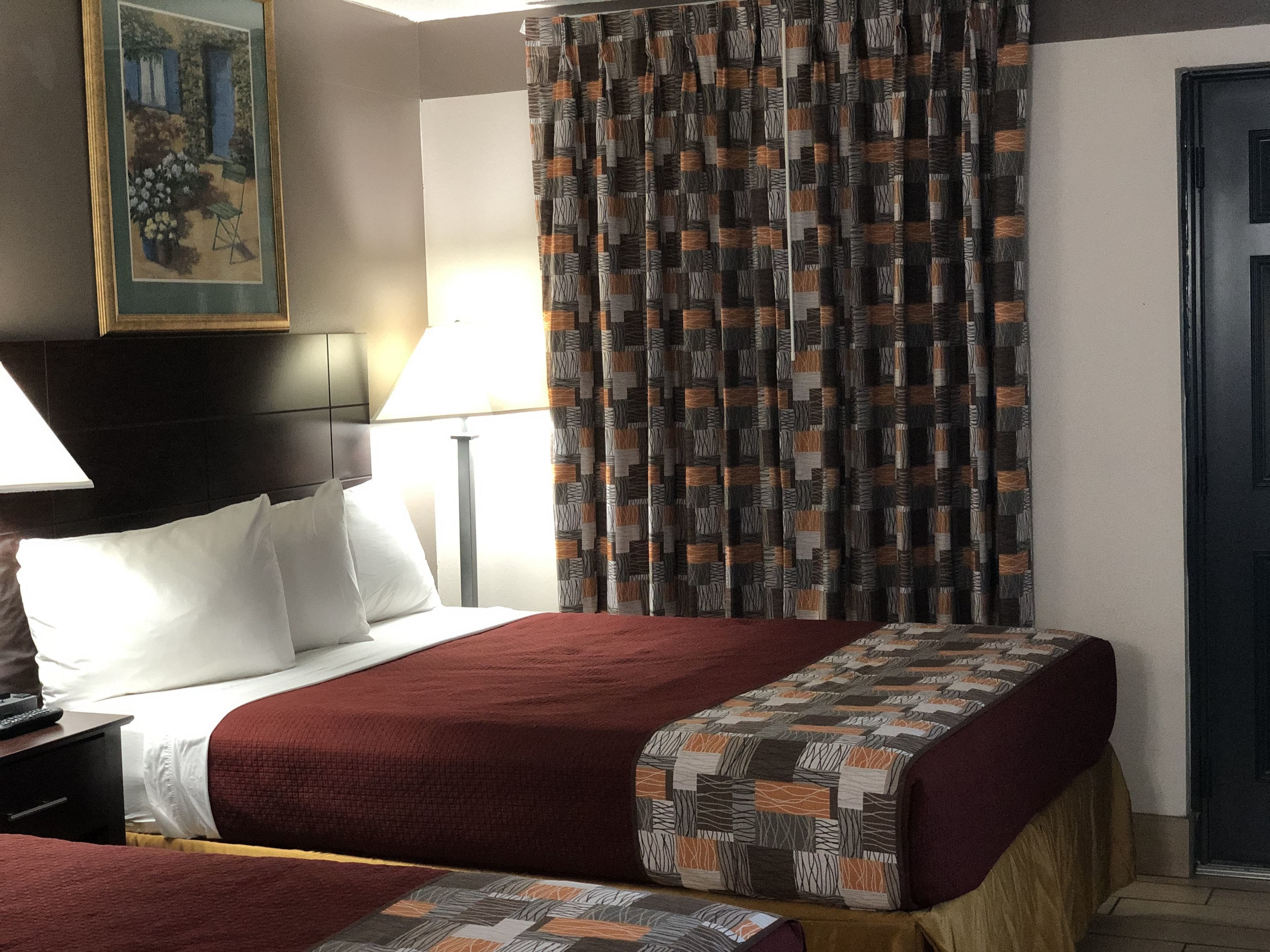 Habitación de hotel con dos camas, un cuadro en la pared, una lámpara y una cortina estampada.