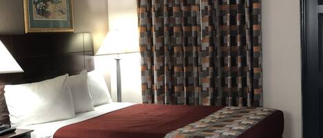 A hotel room with two beds, a painting on the wall, a lamp, and a patterned curtain.