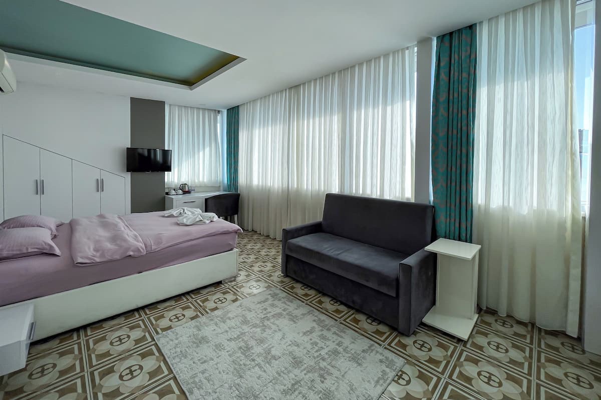 Quarto de hotel com cama, escrivaninha, poltrona, sofá e televisão.