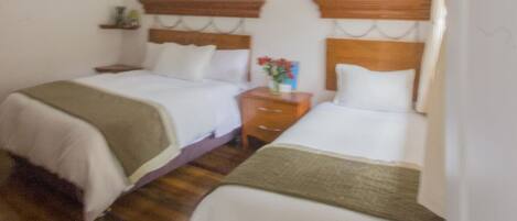 Un dormitorio con dos camas, vigas de madera en el techo, un ventanal pequeño y una mesita de noche con un florero.
