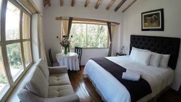 Un dormitorio con una cama, una silla, una mesa con un jarrón de flores y una ventana con cortinas.