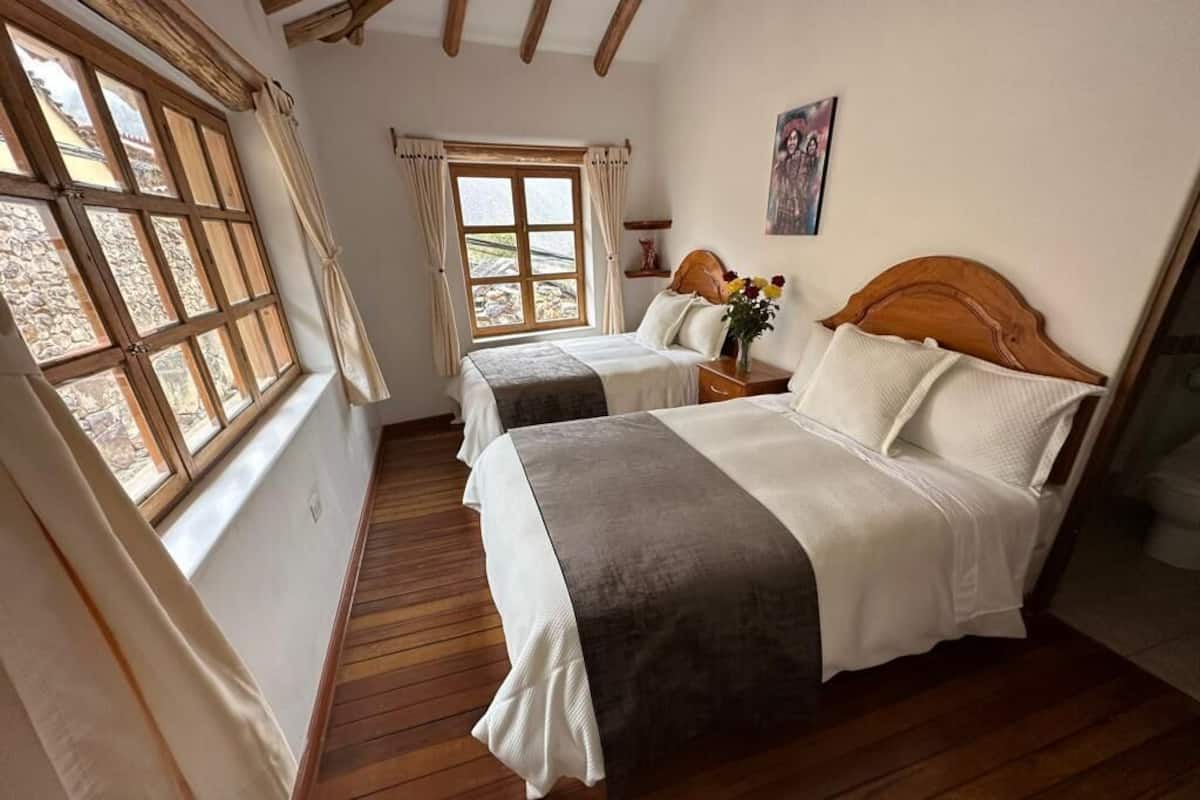Ein Zimmer mit zwei Betten, Holzboden, einem Fenster mit Vorhängen und einem Bild an der Wand.