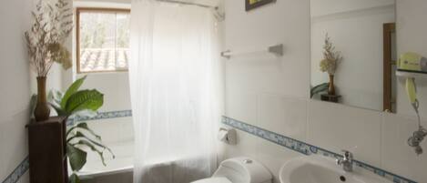 Un baño con inodoro, bidé, lavamanos y una ventana con cortina.