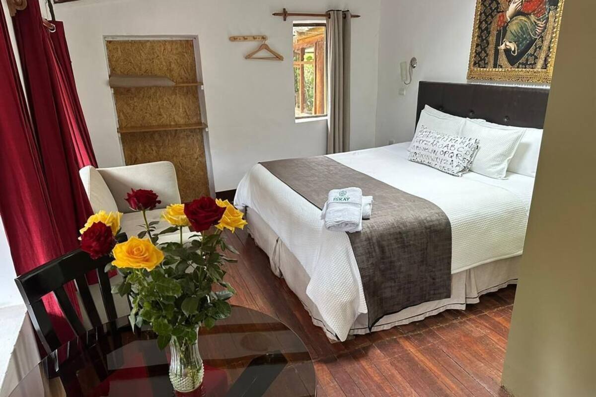 Ein Hotelzimmer mit Bett, Sessel, Tisch mit Blumenvase und Fenster mit Vorhängen.