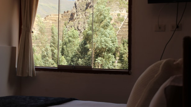 Una habitación con cama, ventana con cortinas y vista a un paisaje montañoso.
