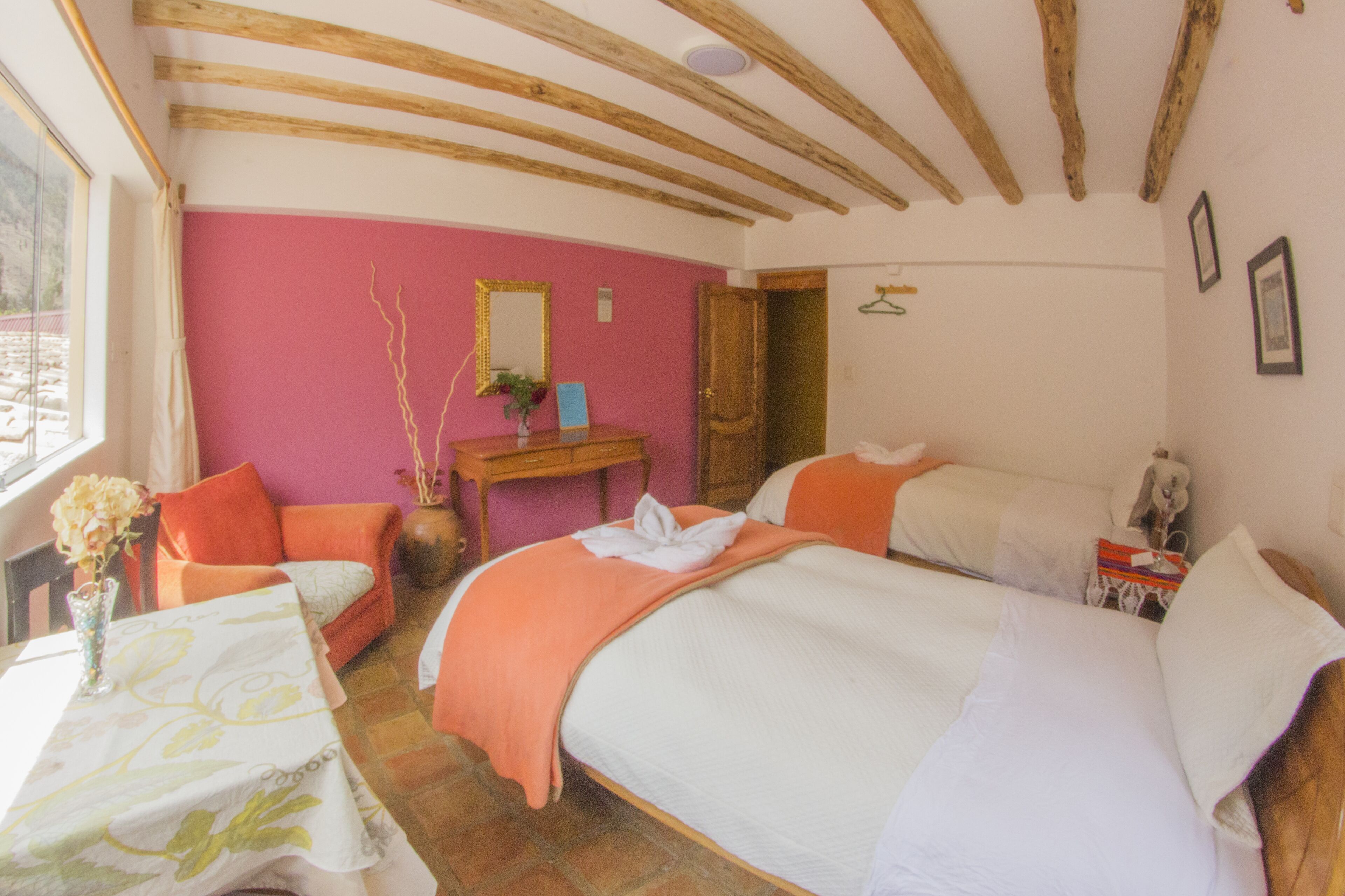 A bedroom with two beds, a wooden ceiling, a pink wall, and a window.