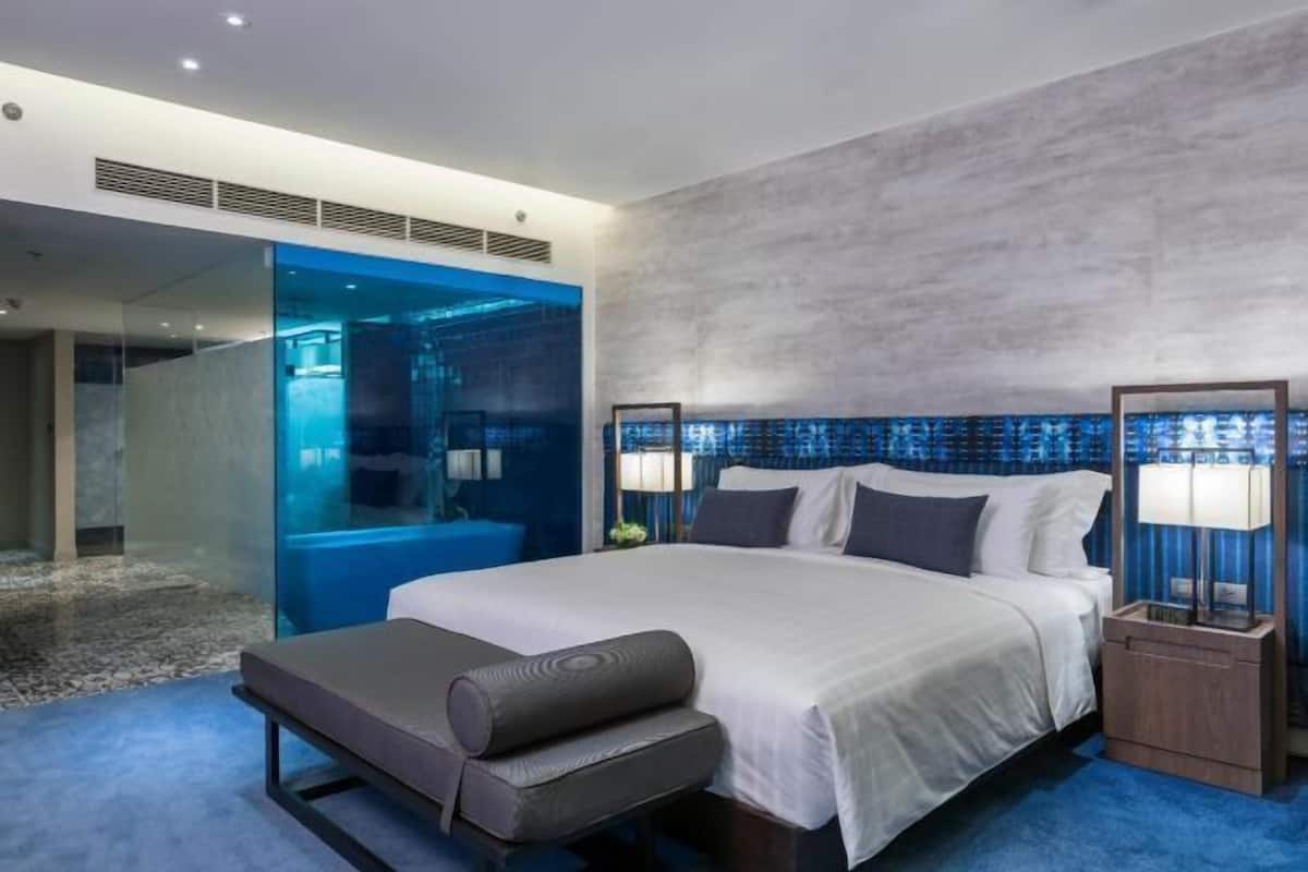 Une chambre d’hôtel moderne avec un grand lit, un banc et une cloison en verre.