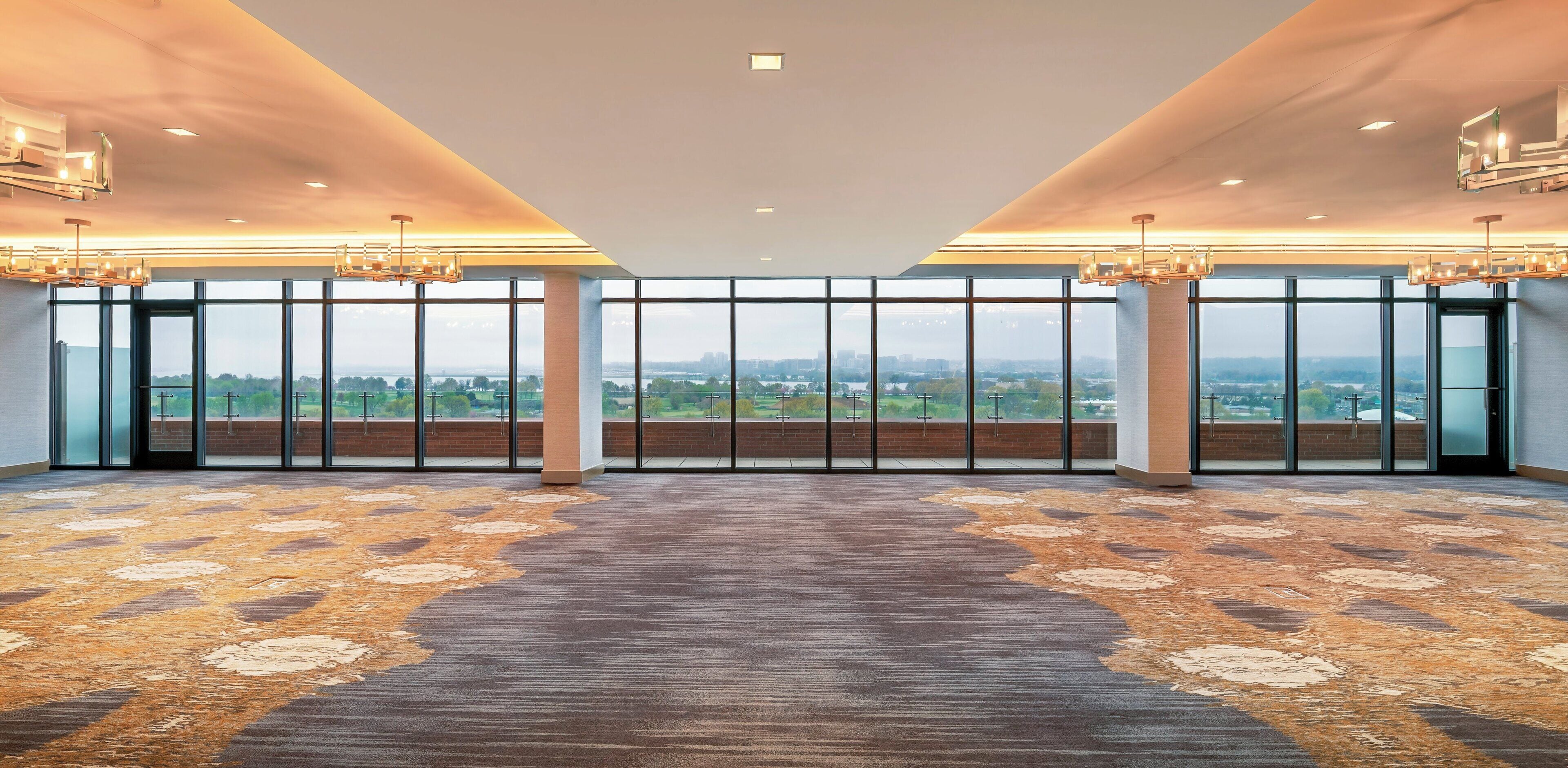 A spacious room with large windows, a patterned carpet, and modern lighting fixtures.