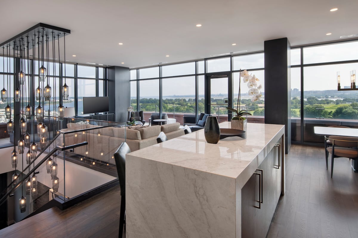 A modern interior with a kitchen island, seating area, and large windows offering a city view.