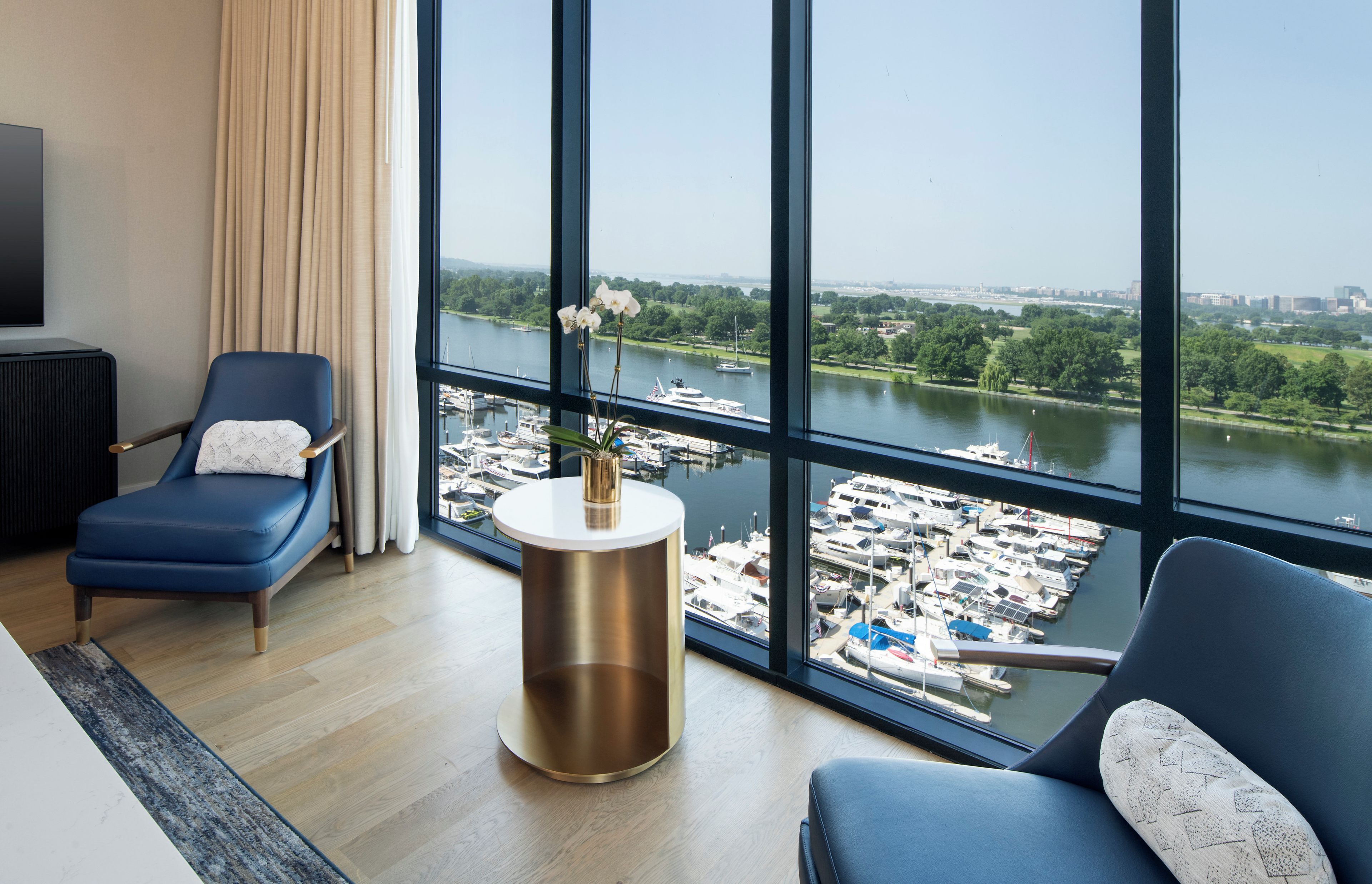 A modern hotel room with a large window offering a view of a marina and city skyline.