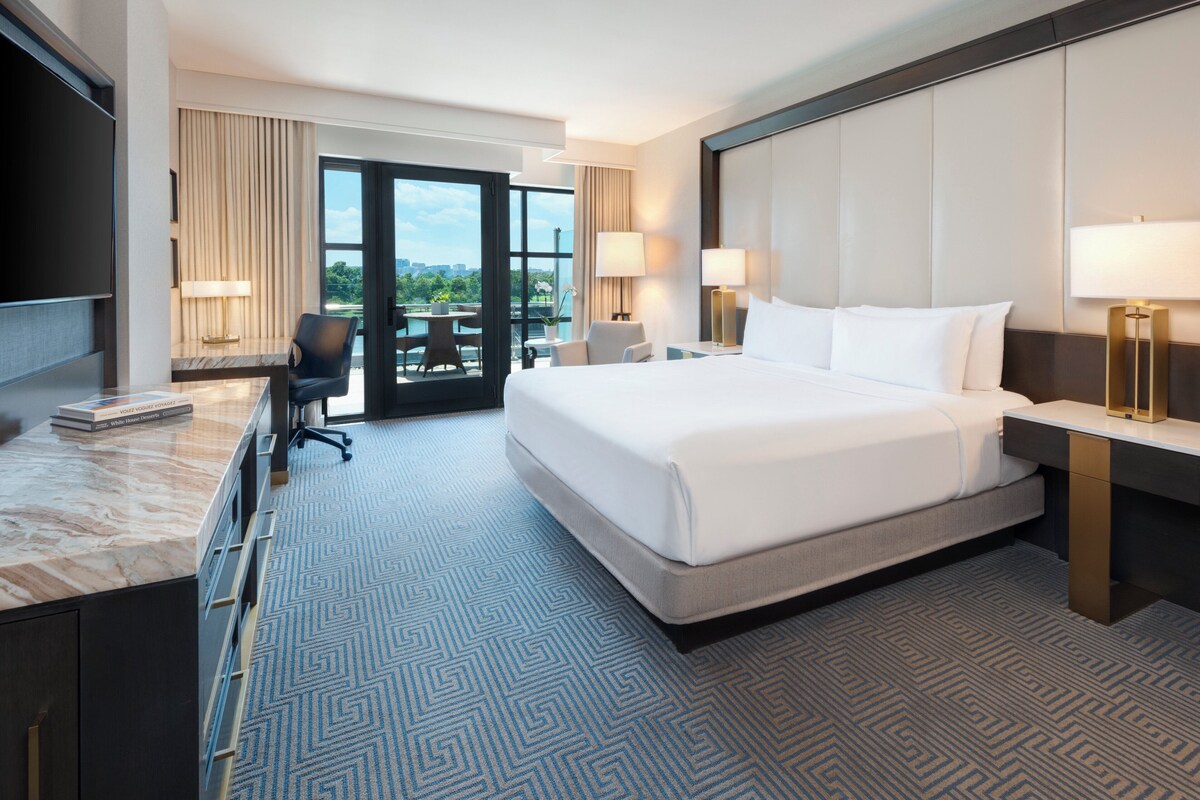 A hotel room with a large bed, a desk with a chair, a TV, and a view of the outdoors.
