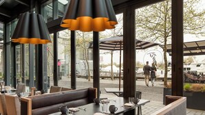 Un restaurante al aire libre con mesas, bancos, ventanas amplias y lámparas colgantes.