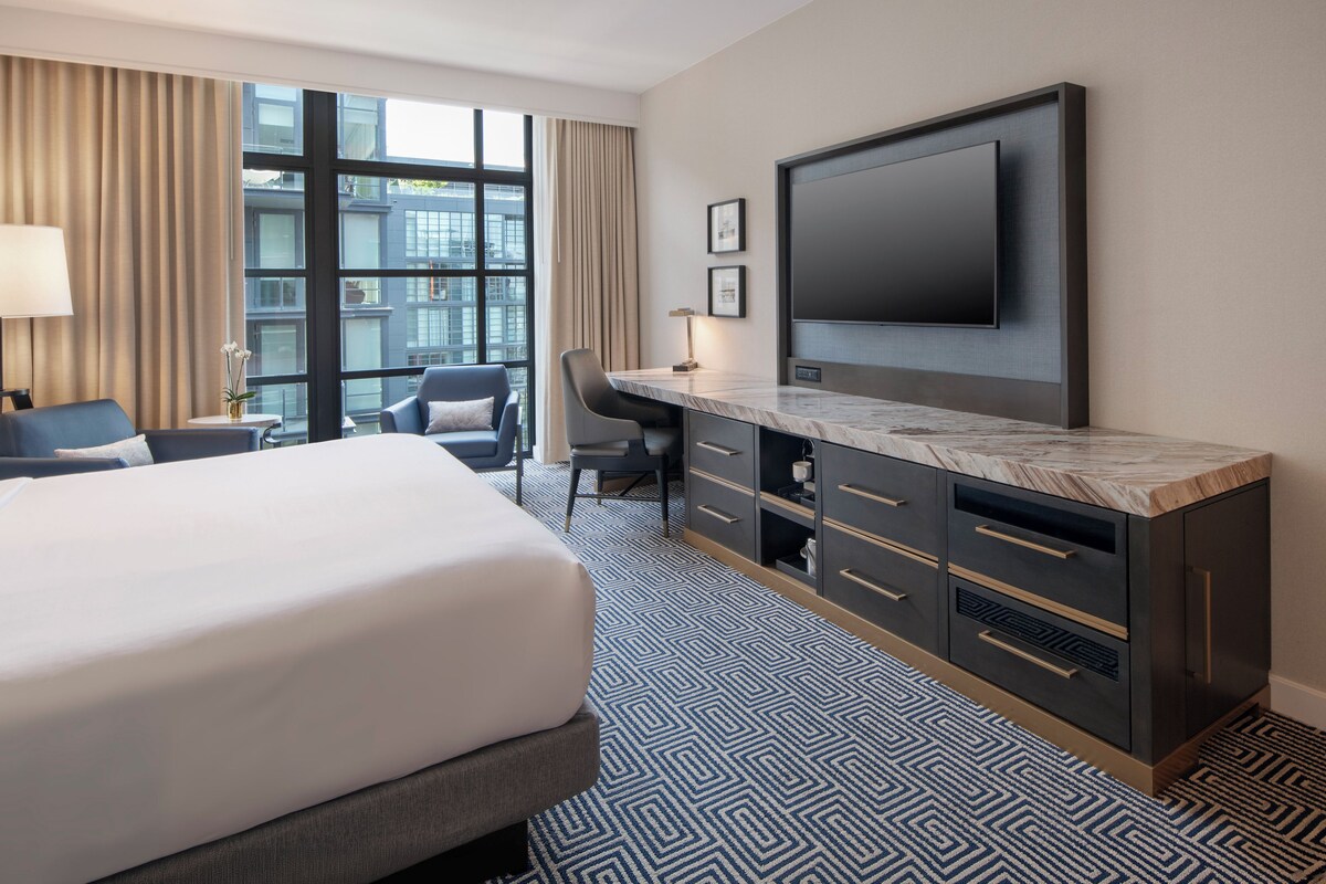 A hotel room with a large bed, a desk, a chair, a television, and a window with curtains.
