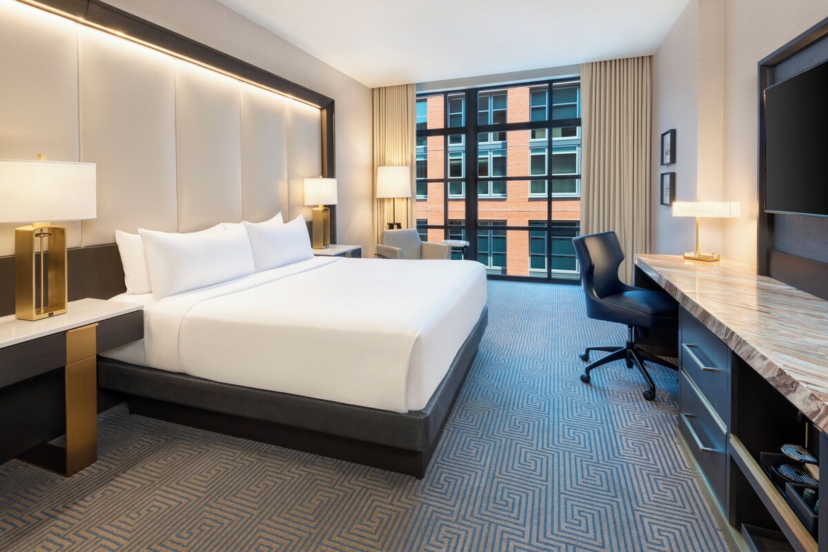 A hotel room with a large bed, a desk, a chair, and a TV.