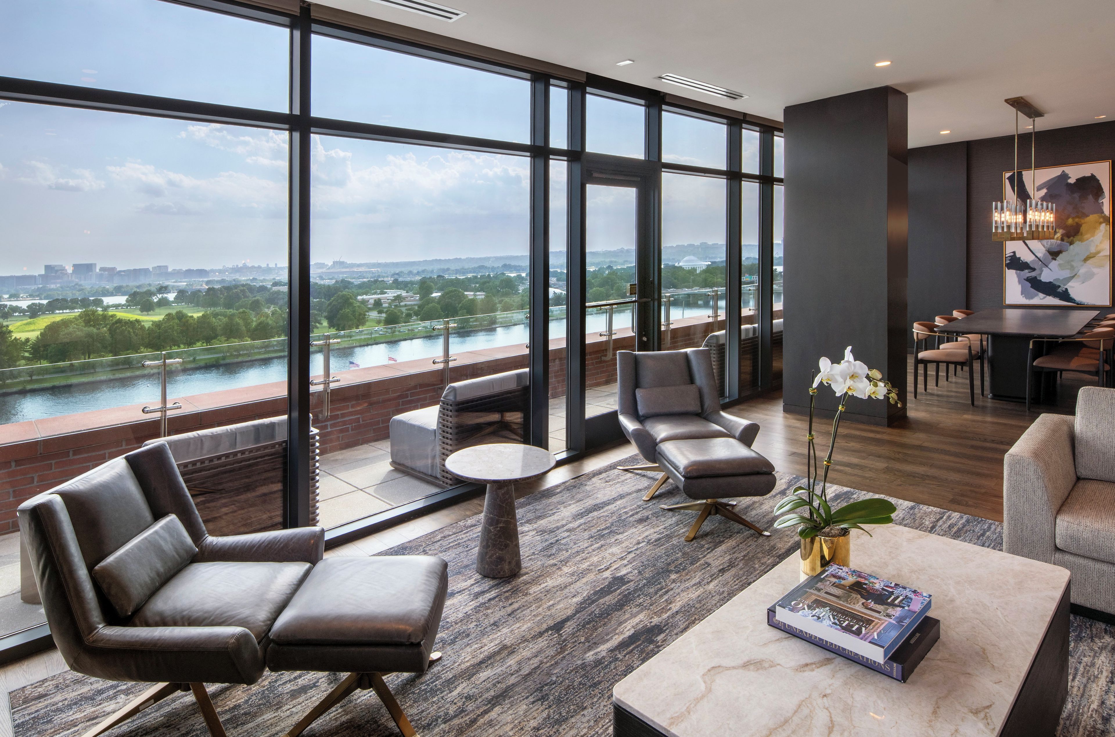 A modern hotel lobby with leather seating, a coffee table, and a view of a river and cityscape through large windows.