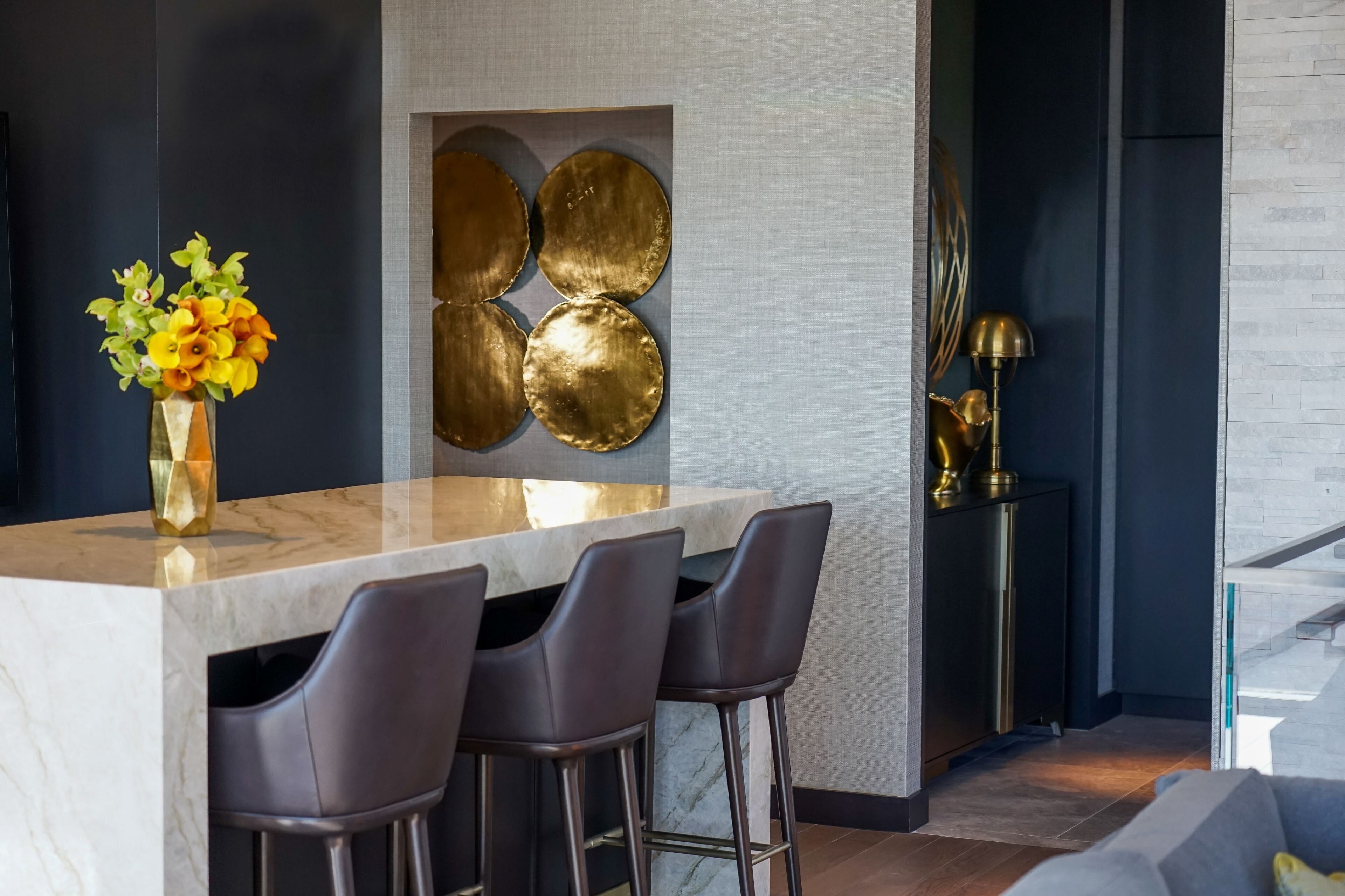 Une cuisine moderne avec un plan de travail en marbre, des tabourets de bar, un vase de fleurs et des œuvres d’art décoratives au mur.