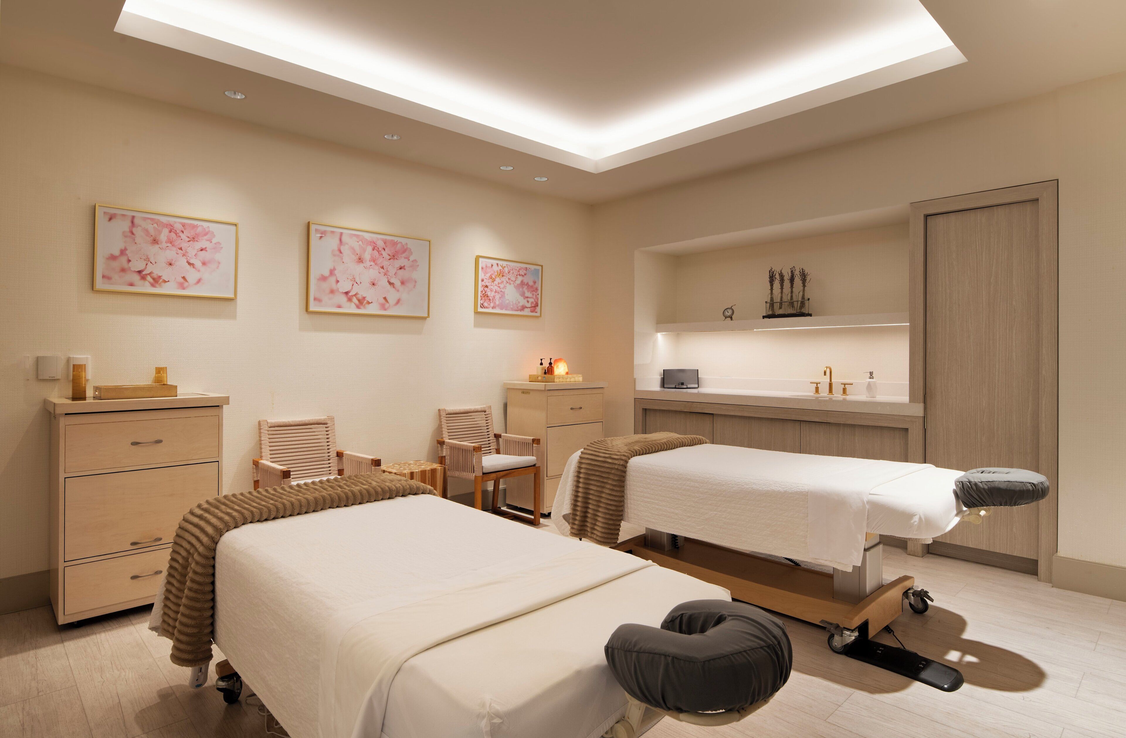 Een moderne hotelkamer met twee bedden, een massagetafel, een bureau en een kaptafel met planken.