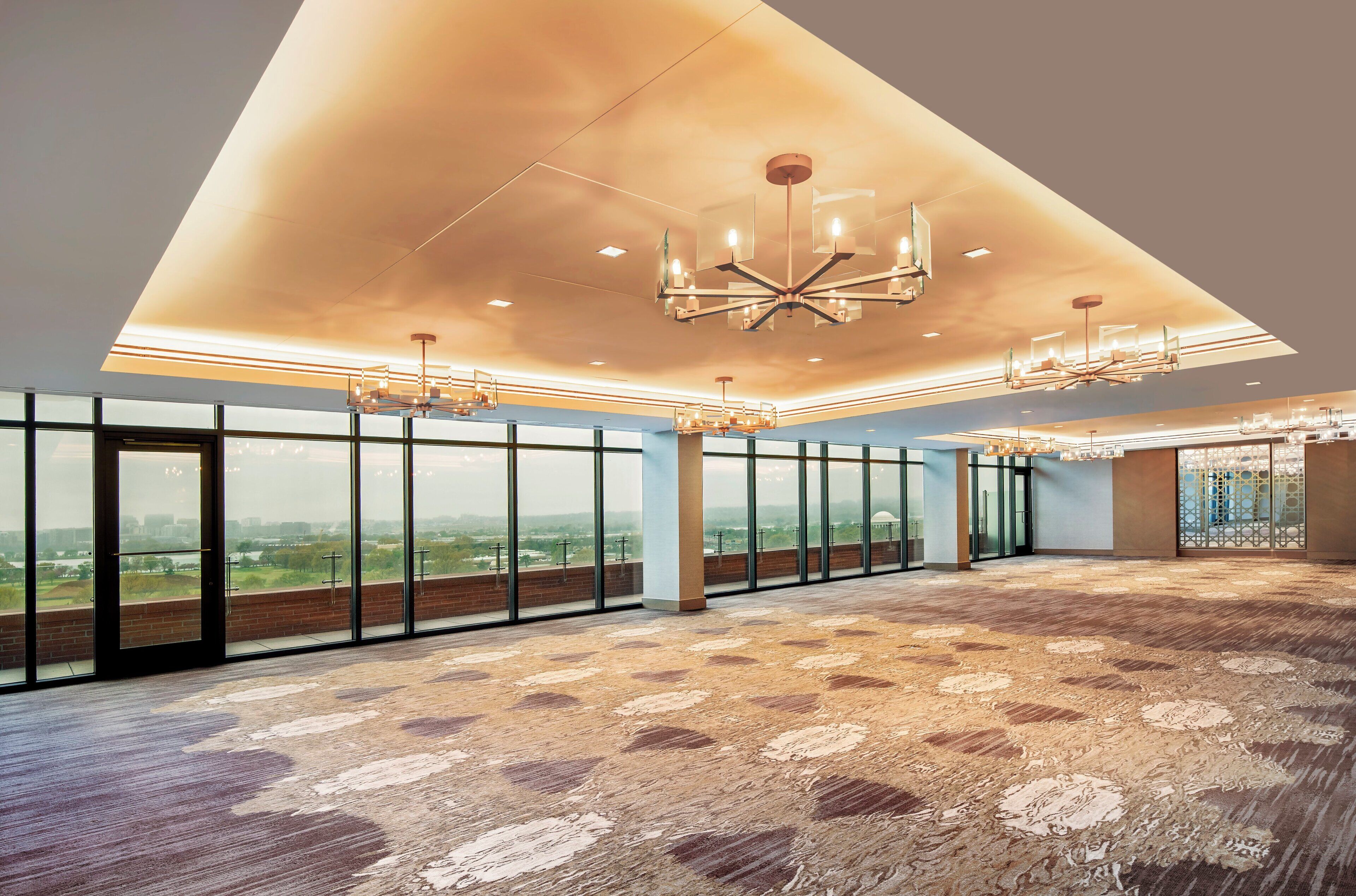 A spacious room with large windows, a patterned carpet, and multiple chandeliers.