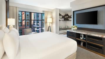 Une chambre d’hôtel moderne dotée d’un grand lit, d’un téléviseur à écran plat, d’un bureau avec un ordinateur et offrant une vue sur le paysage urbain.