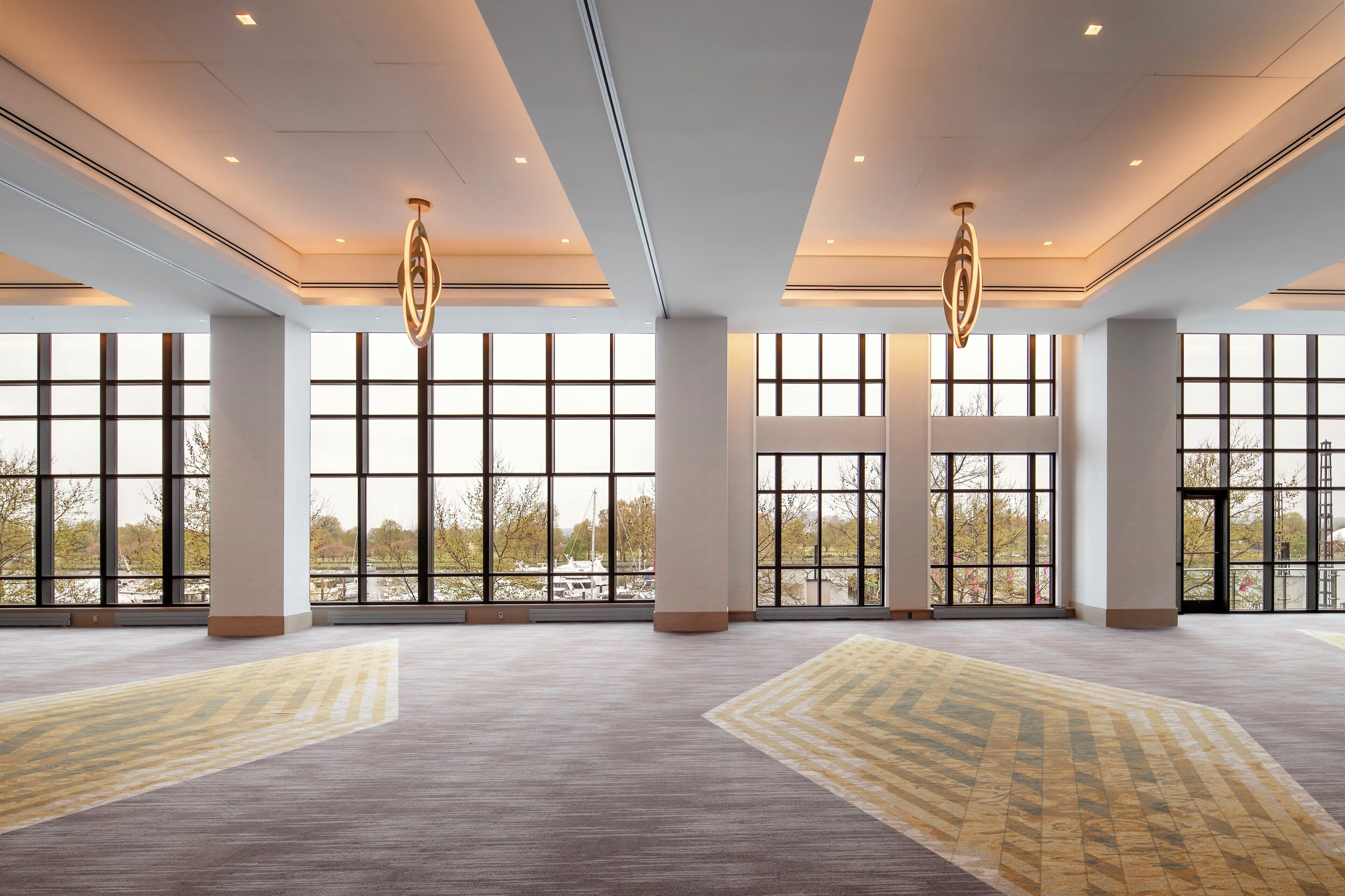 A spacious hotel lobby with large windows, a high ceiling, and modern lighting fixtures.