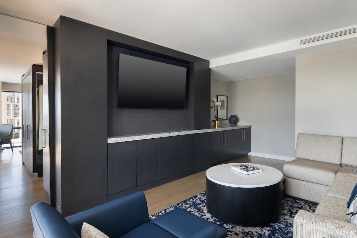 A modern living room with a flat-screen TV mounted on a dark wall, a round coffee table, and a sofa with a patterned rug.