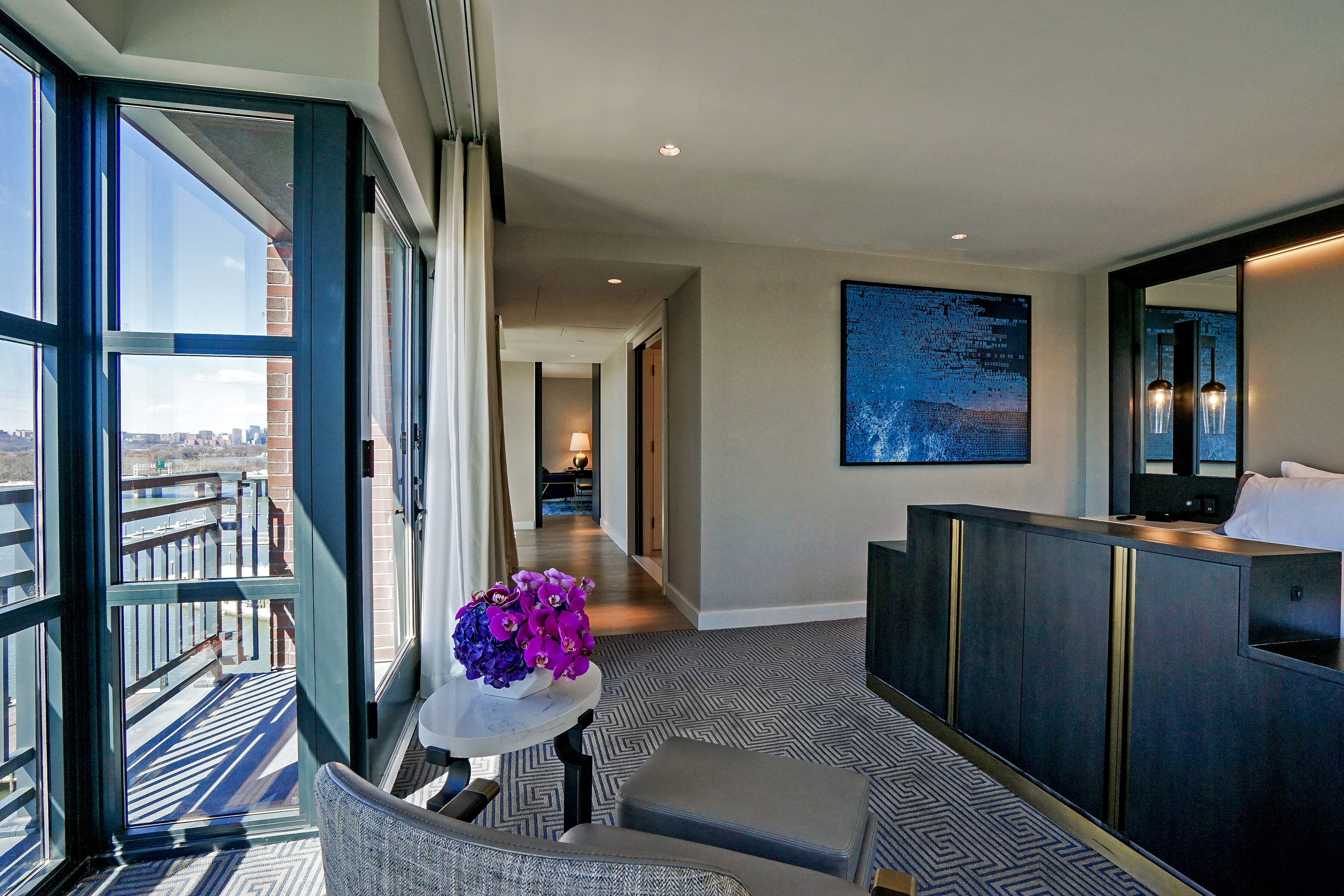 A hotel room with a view of the city, a large window, a seating area, and a modern bathroom.