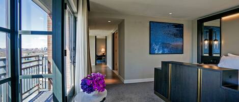 A hotel room with a view of the city, a large window, a seating area, and a modern bathroom.