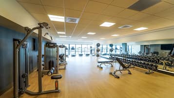 A gym with exercise equipment, a mirror wall, and a wooden floor.