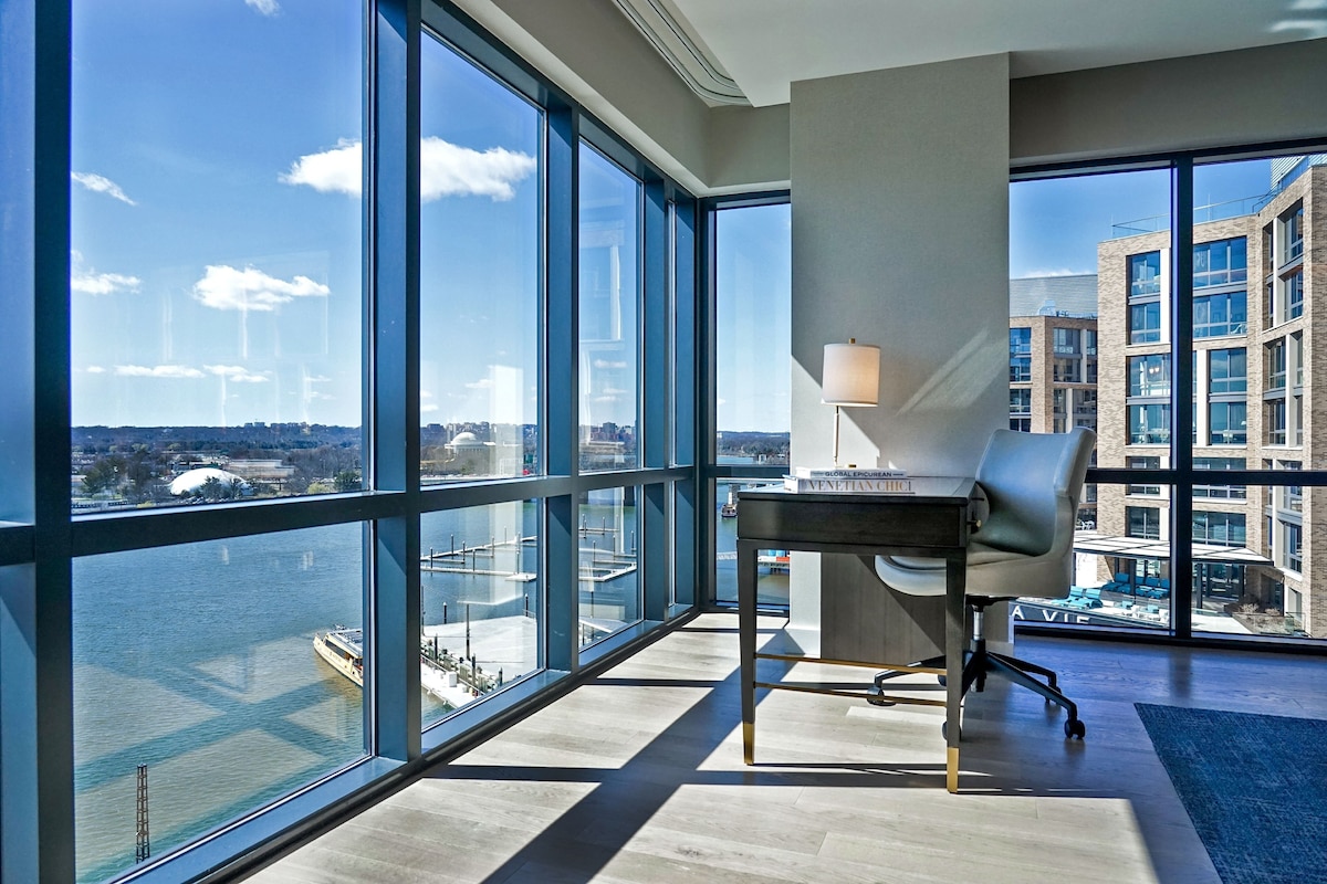 A modern office space with large windows, a desk, and a lamp.