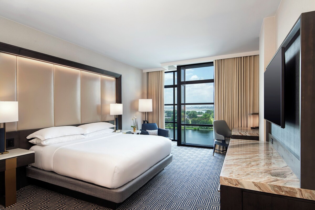 A modern hotel room with a large bed, a desk, a chair, and a TV.