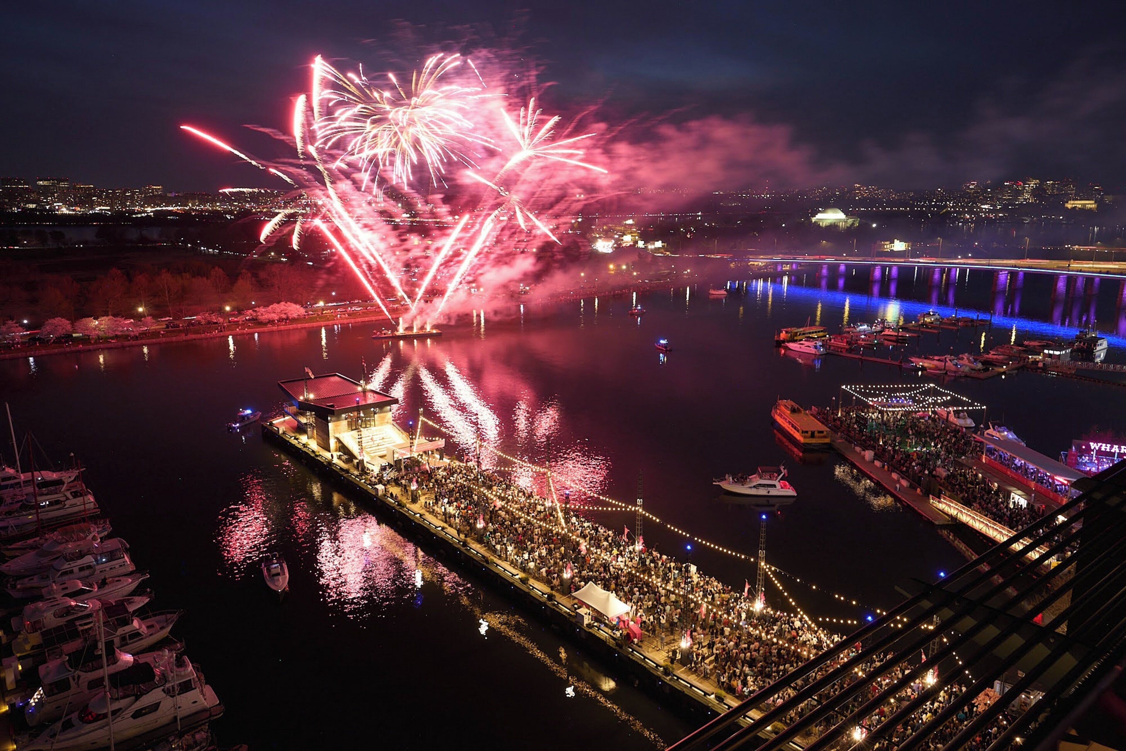 Uma área à beira-mar com barcos, pessoas e fogos de artifício.