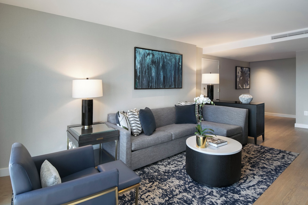 A modern living room with a grey sofa, a blue armchair, a round coffee table, and two side tables with lamps.