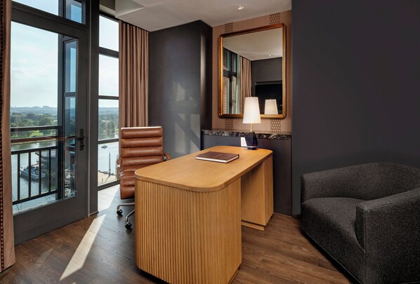 A hotel room with a desk, a chair, a sofa, a large mirror, and a view of a body of water through a window. - InterContinental Washington D.C. - The Wharf by IHG (Washington)