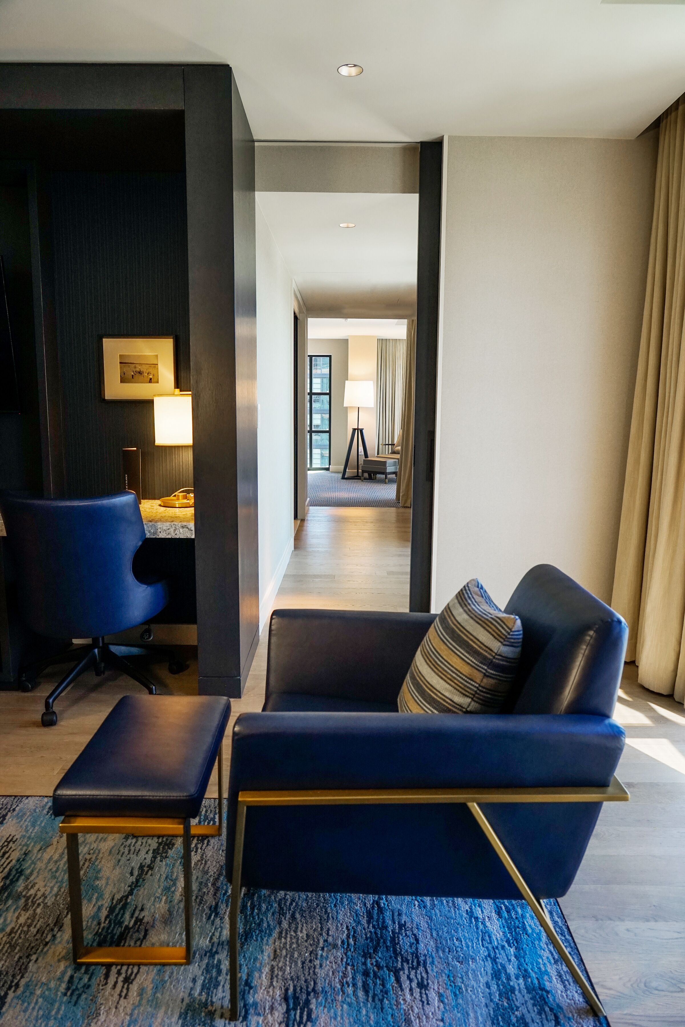 A modern hotel room with a blue sofa, a desk with a chair, and a lamp.