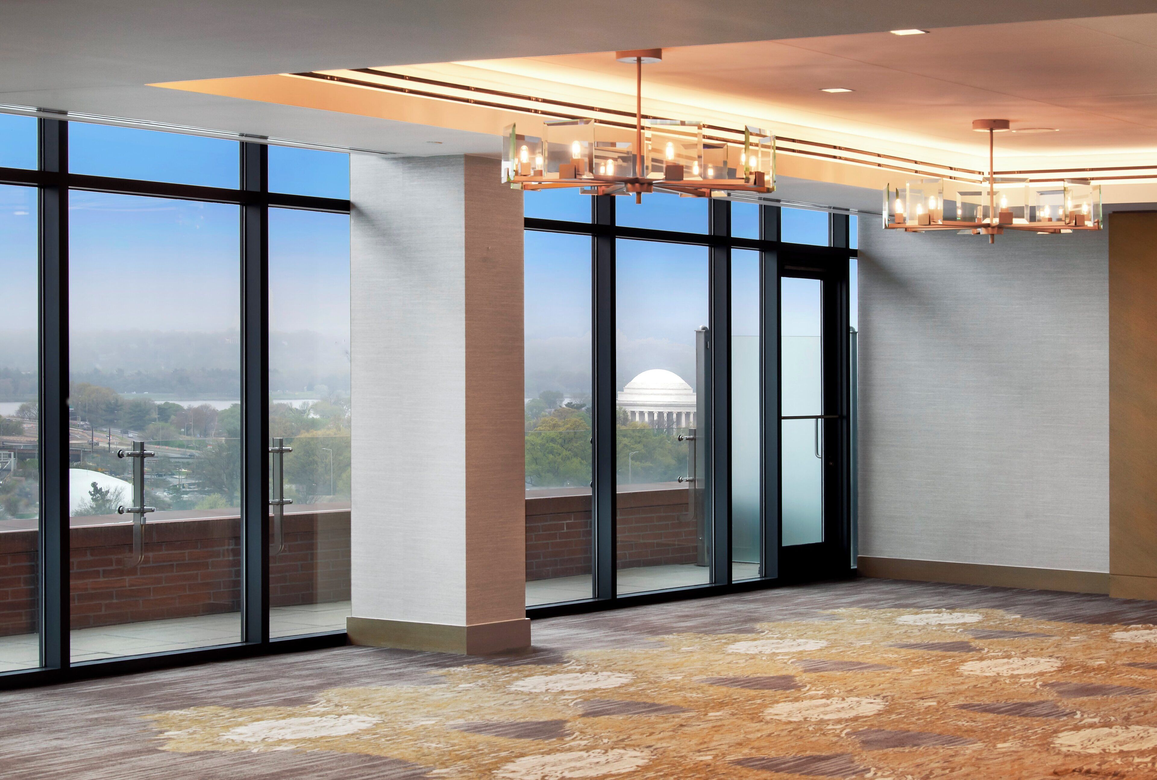 A spacious room with large windows, a patterned carpet, and a modern chandelier.