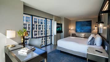 A hotel room with a bed, desk, chair, TV, and large windows.