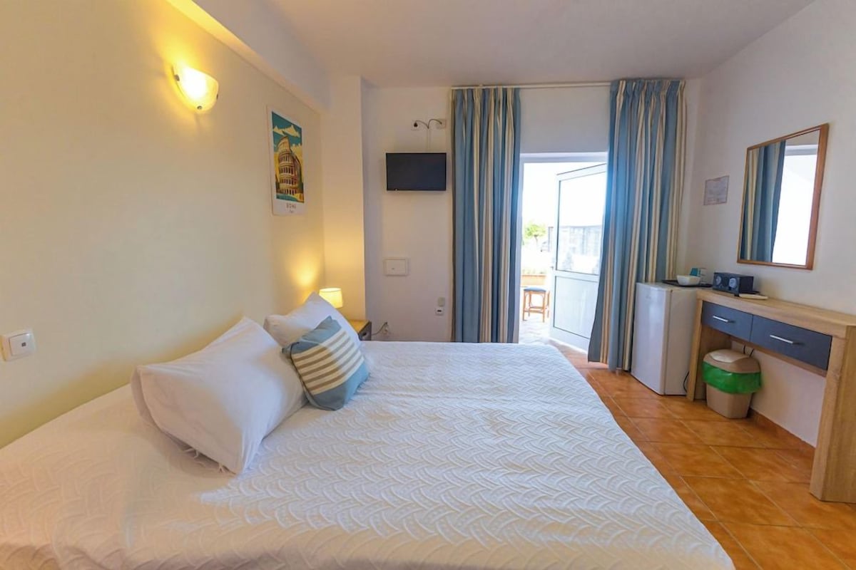 A hotel room with a bed, a desk, a chair, a television, and a window with curtains.