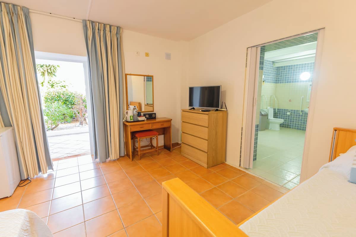 Habitación de hotel con cama, escritorio con silla, televisor, armario y baño visible a través de una puerta abierta.