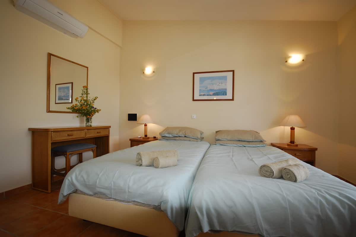 Una cama doble con dos almohadas, una mesita de noche con lámpara, un escritorio con silla y un aire acondicionado instalado en la pared.
