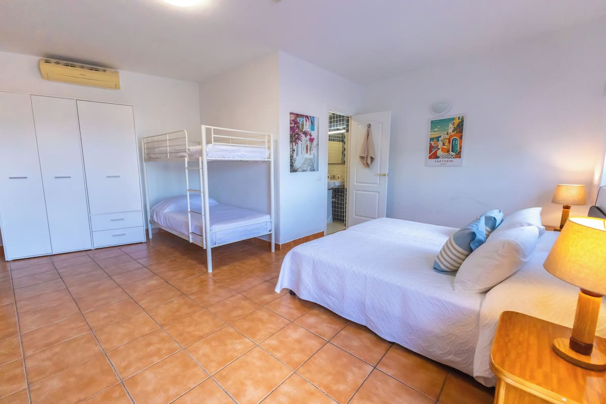 Un dormitorio con una cama litera, una cama individual, un armario y una puerta que da al baño.