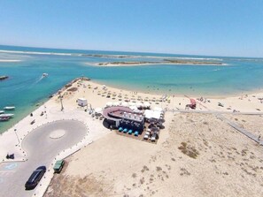 An aerial view of a beachside property with a circular driveway, a bar/lounge area, and a sandy beach with umbrellas.