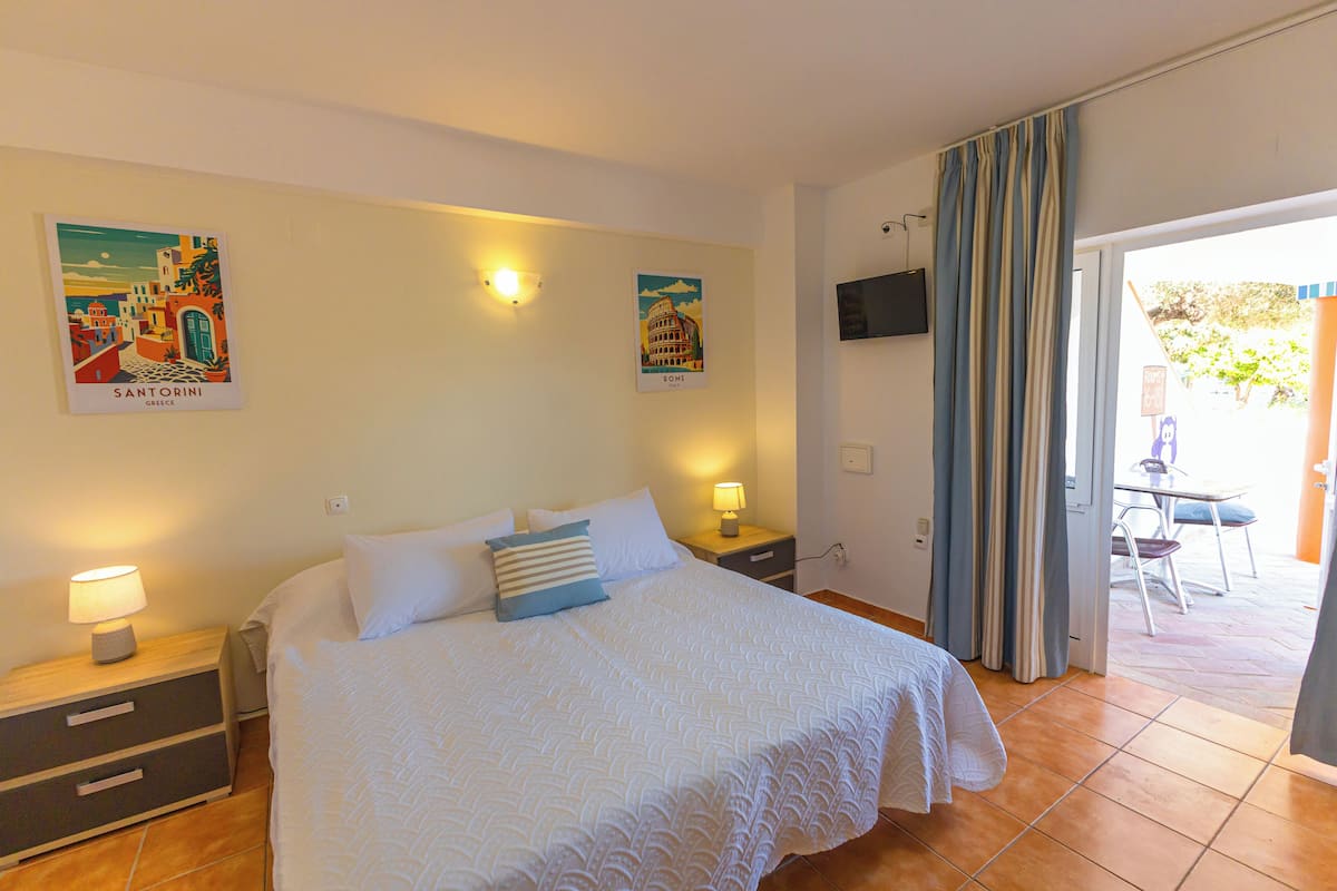 Un dormitorio con cama, mesitas de noche, televisor y dos lámparas de pared.