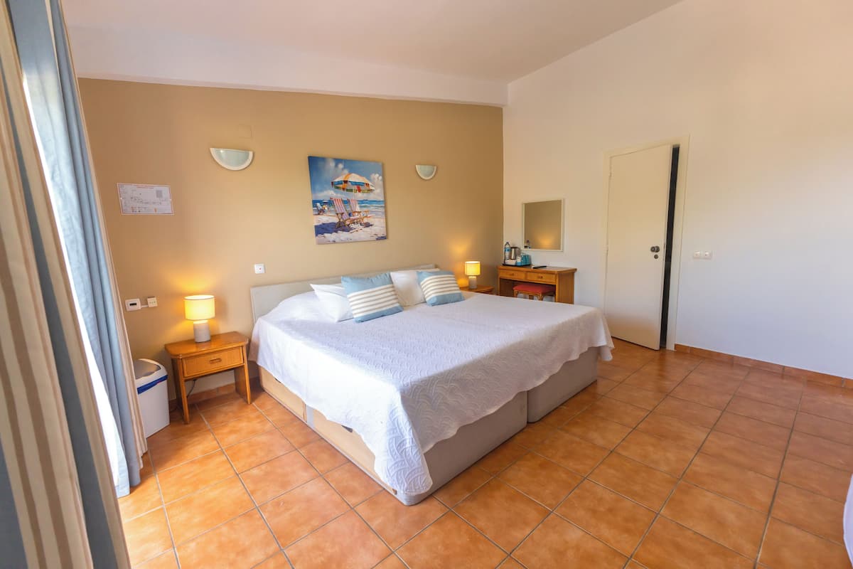 Un dormitorio con una cama, lámparas de noche, una mesita de noche, un cuadro, un espejo y una puerta.