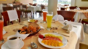 Un desayuno preparado para dos personas, con una mesa que incluye un plato de fruta, una cesta de pasteles, un vaso de zumo de naranja y una taza de café.