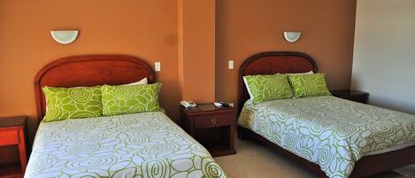 Dos camas matrimoniales con ropa de cama verde estampada, cabeceros de madera, mesitas de noche con lámparas y apliques de pared.