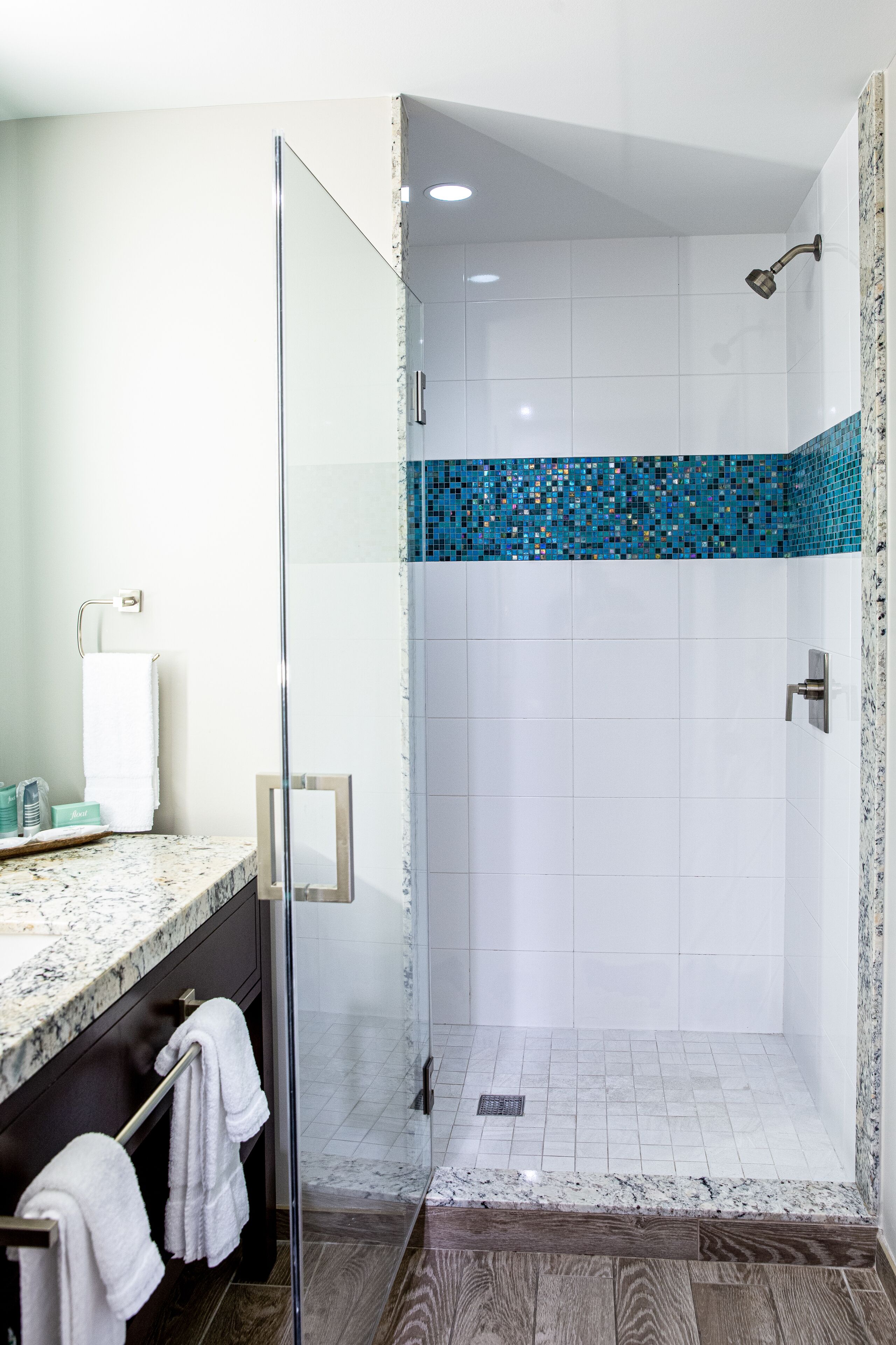 A modern bathroom with a glass shower enclosure, white tiles, and a blue mosaic border.