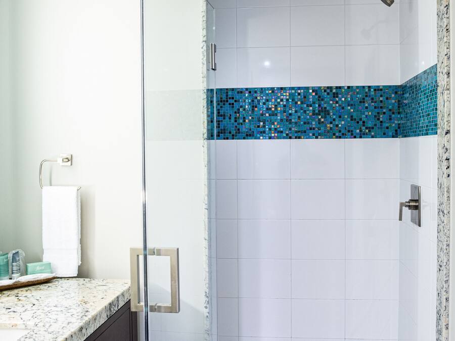 Un baño moderno con cabina de ducha de vidrio, azulejos blancos y un borde de mosaico azul.