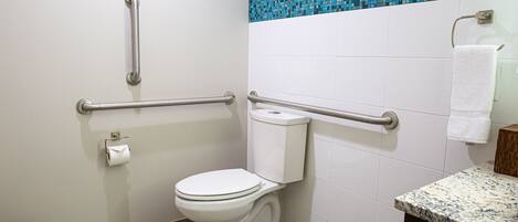 A bathroom with a white toilet, grab bars, a blue mosaic tile backsplash, and a marble countertop.