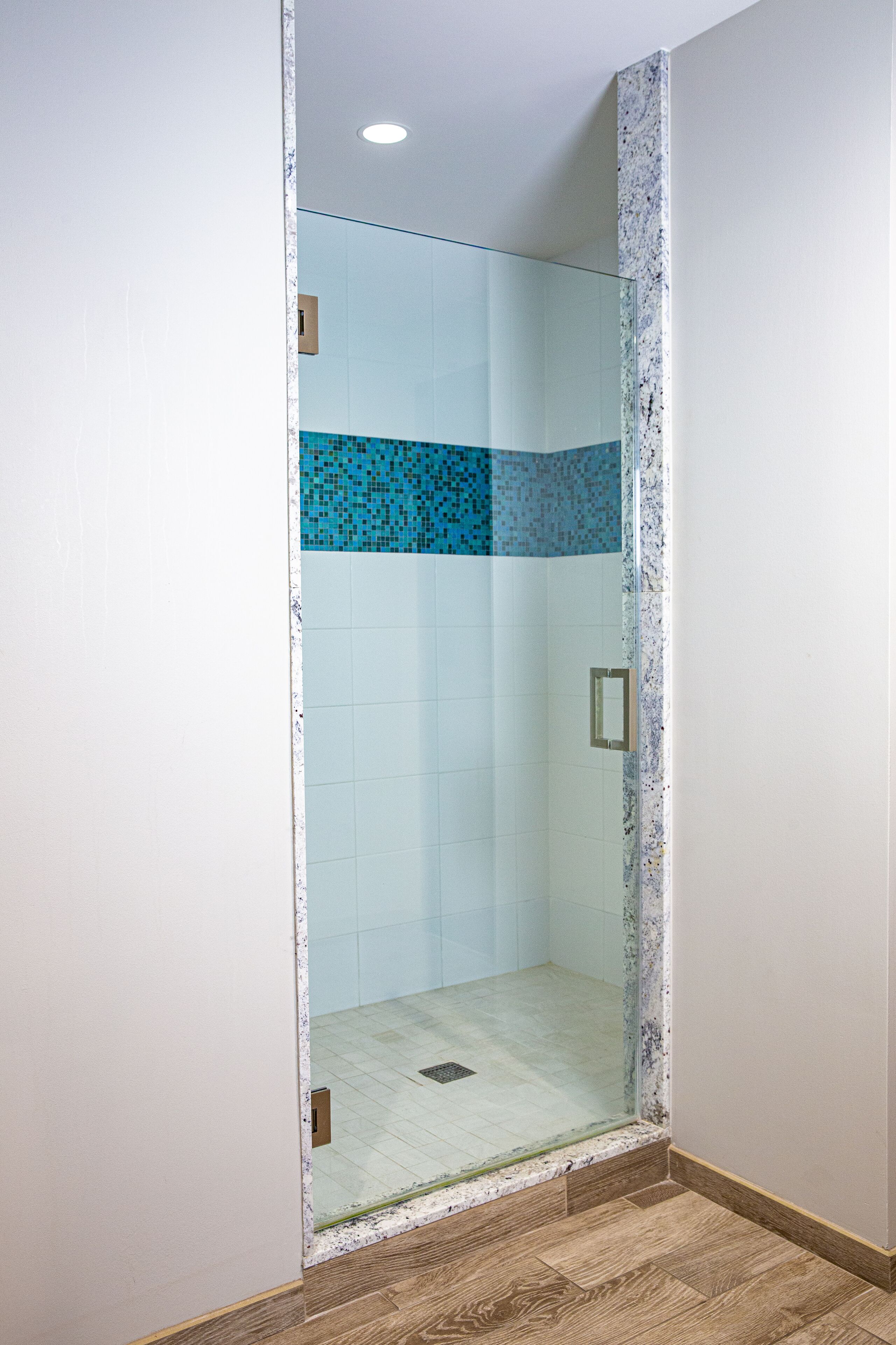 A glass-enclosed shower with blue mosaic tiles and a wooden floor.