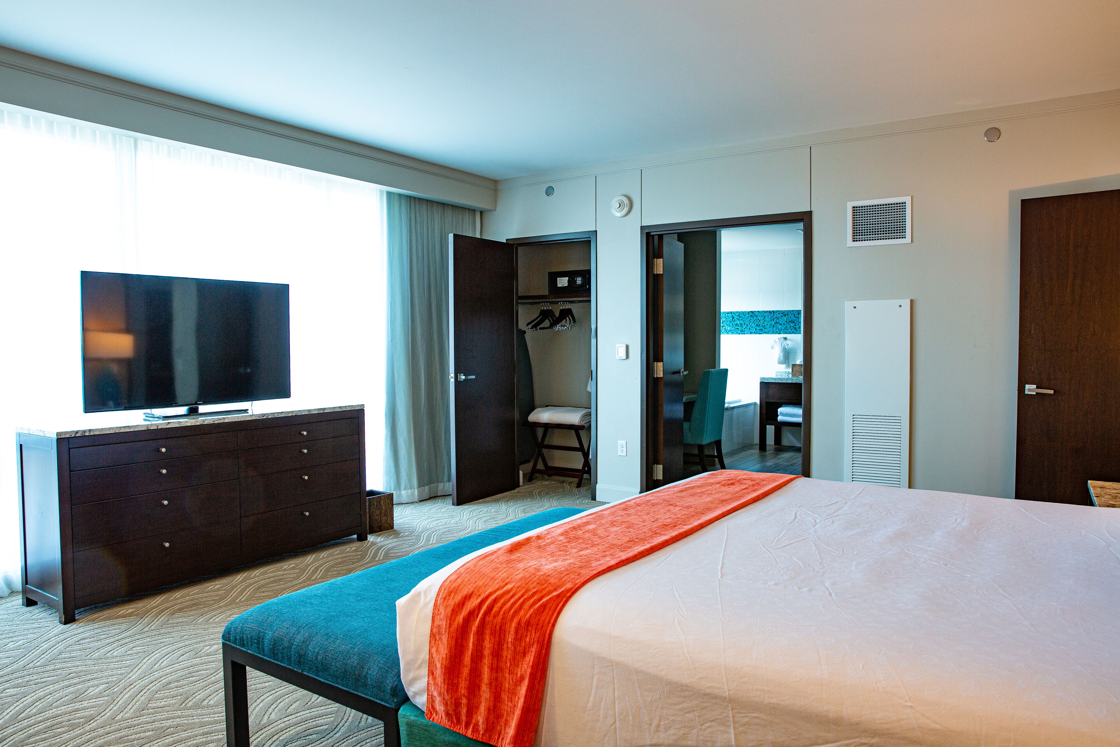 A hotel room with a bed, a television, a dresser, and a desk.